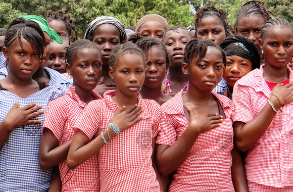 En grupp skolflickor i rutiga skjortor håller handen på hjärtat