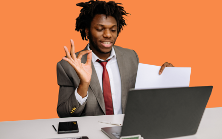 Person som sitter med dator och håller ett papper och gör ett "toppentecken"med händerna