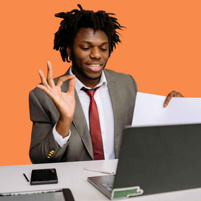 Person som sitter med dator och håller ett papper och gör ett "toppentecken"med händerna