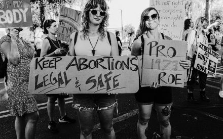 Svartvit bild där två kvinnor håller i plakat. Texten säger Keep abortions legal and safe.