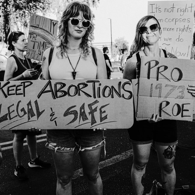 Svartvit bild där två kvinnor håller i plakat. Texten säger Keep abortions legal and safe.