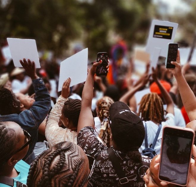 Människor protesterar med skyltar och filmar med sina mobiler.