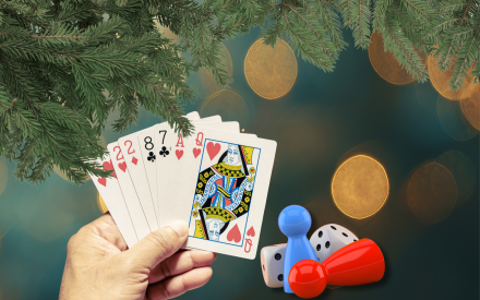 Collage, en hand som håller i spelkort, spelpjäser och en tärning. Gran och glitter i bakgrunden.