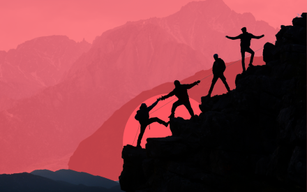 Fyra människor hjälper varandra uppför ett berg mot en rosaröd himmel.