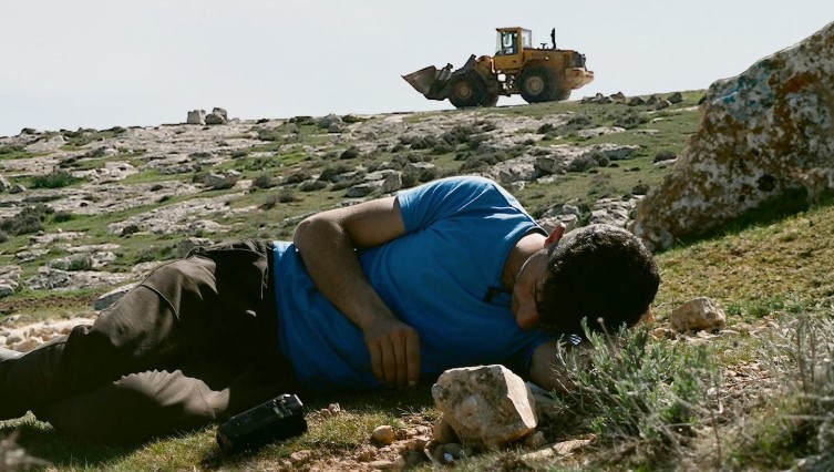 Man ligger i en grässluttning. I bakgrunden syns en grävmaskin.