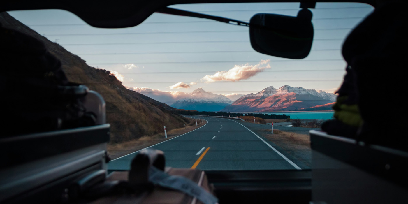 Foto från en framruta på en bil som åker på en landsväg i bergen.