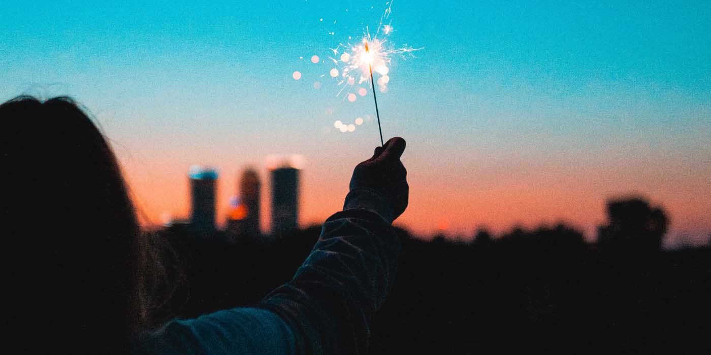 Tjej håller upp ett tomtebloss i en solnedgång