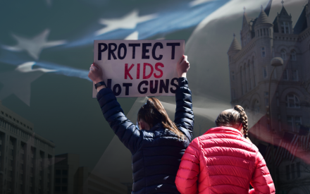 Demonstrant håller upp plakat med texten Protect kids not guns. USA:s flagga i bakgrunden