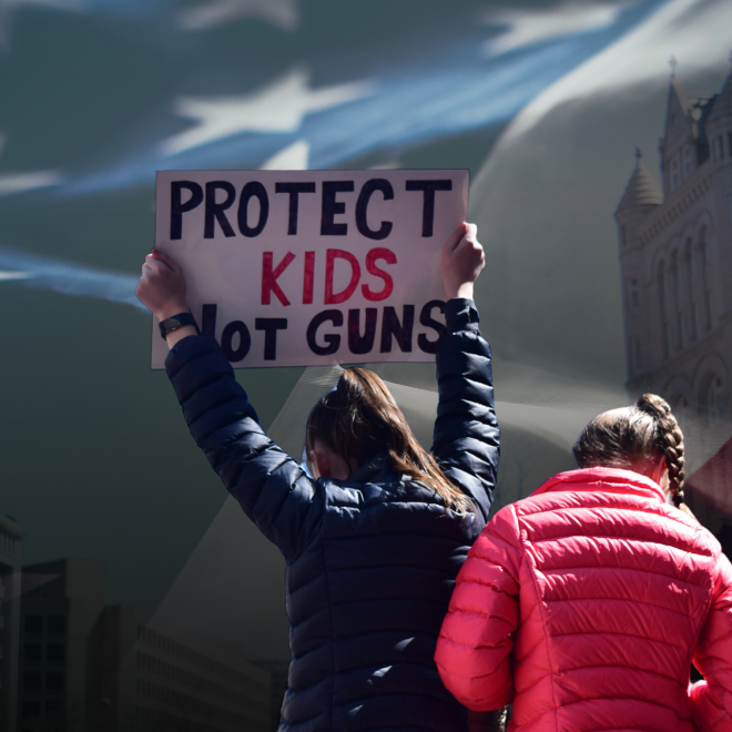 Demonstrant håller upp plakat med texten Protect kids not guns. USA:s flagga i bakgrunden