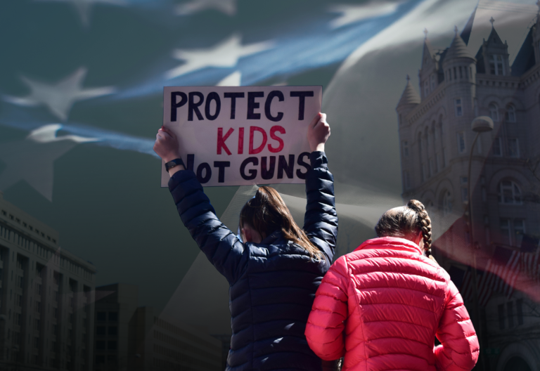 Demonstrant håller upp plakat med texten Protect kids not guns. USA:s flagga i bakgrunden