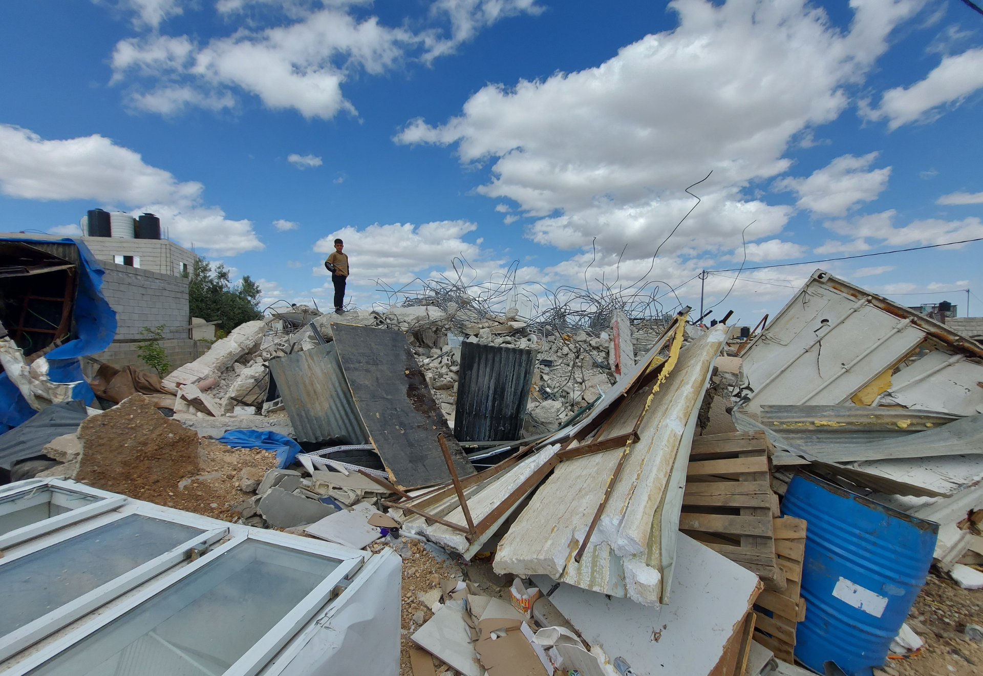 En pojke står på ruinerna av sitt hem.