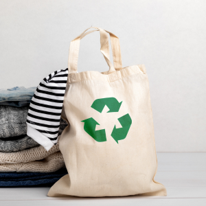 Bild på tygkasse med återvinningstecken och en hög kläder.