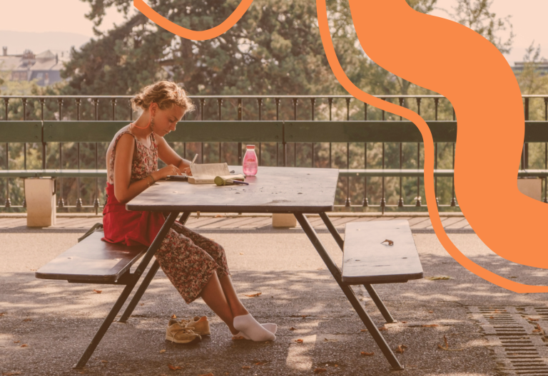 Tjej som sitter ute vid en bänk och pluggar