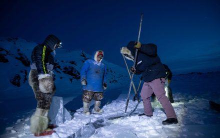 "WWF staff, Erica Guth (in purple pants), tries her hand at breaking off a chunk of lake ice by continuously driving the pick into the thick ice at an angle. As local Inuit Guardians stand by, a final satisfying blow dislodges a large chunk ready to be harvested and brought back for the Elders to make tea with."