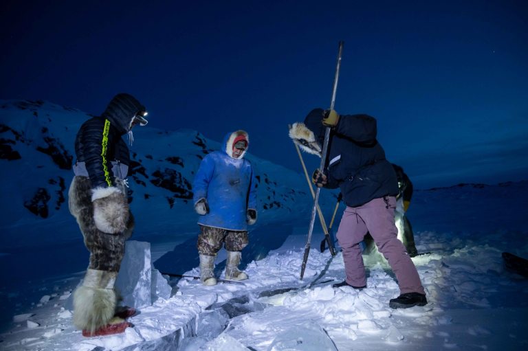 "WWF staff, Erica Guth (in purple pants), tries her hand at breaking off a chunk of lake ice by continuously driving the pick into the thick ice at an angle. As local Inuit Guardians stand by, a final satisfying blow dislodges a large chunk ready to be harvested and brought back for the Elders to make tea with."