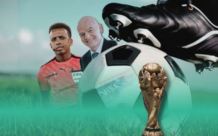 Två män inklippta bakom en fotbollsko på en fotboll och en vm byst