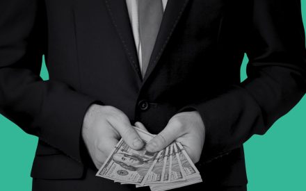Person i kostym håller i en bunt dollar i sina händer