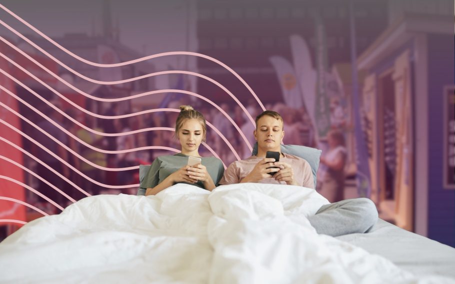 två personen sitter med sina telefoner i sängen. Bakom syns valstugor.